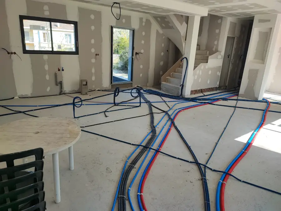 maison en construction, gaines électriques et tuyaux d'eau sont installés au sol sur la dalle, le placo est posé également